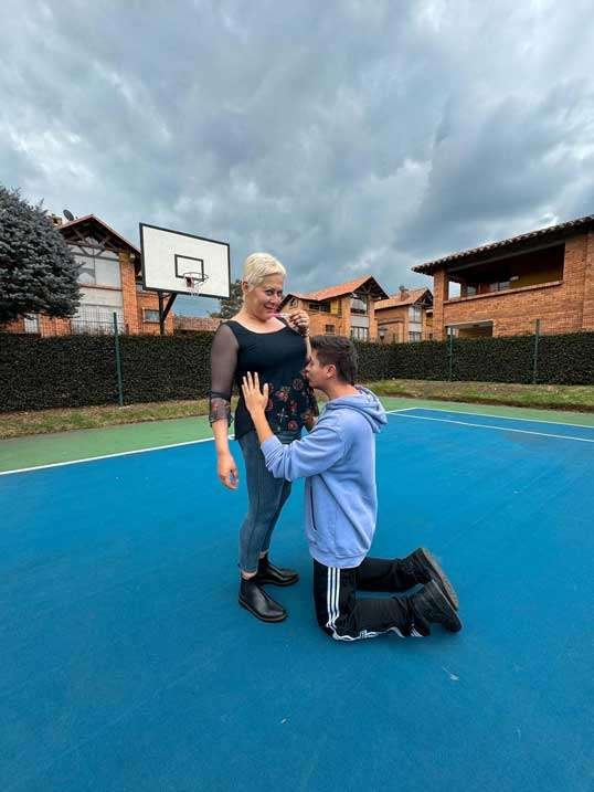 Alina Lozano de pie y su esposo Jim Velásquez de rodillas besando su vientre por su embarazo.