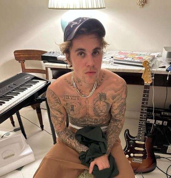 Justin Bieber, famoso cantante sentando sin camisa en un estudio junto a una guitarra y un piano