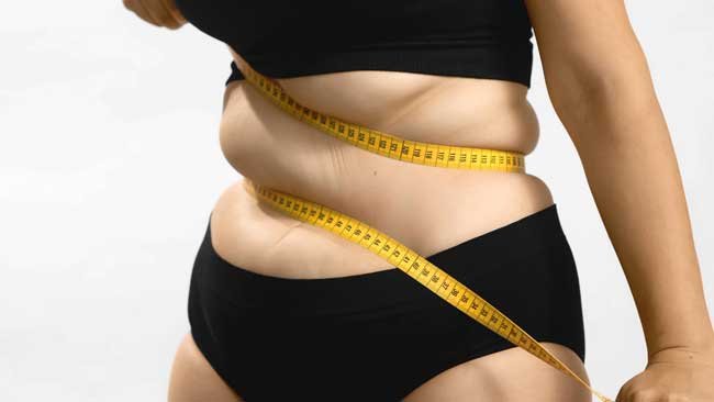 Una mujer de pie con un metro alrededor de su abdomen.
