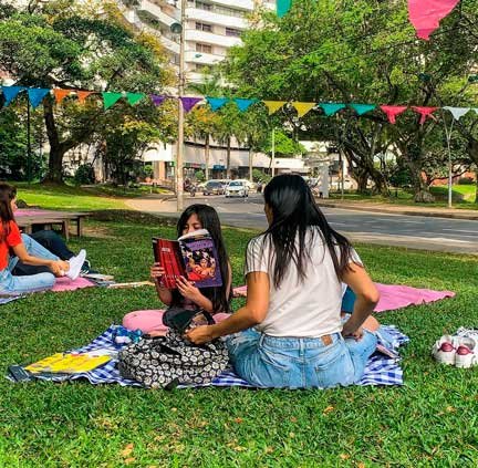 Una madre y su hija sentadas en el jardín del Museo La Tertulia en Cali, leyendo un libro, durante un picnic literario.