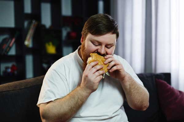 Un hombre con obesidad comiendo una hamburguesa