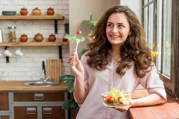 Una joven mujer sostiene un tazón con ensalada de verduras, sinónimo de una alimentación saludable.