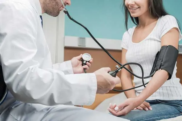 Un médico le toma la presión a una mujer que está sentada.