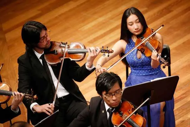 Tres miembros de la Orquesta Filarmónica Juvenil de Bogotá tocando el violín.