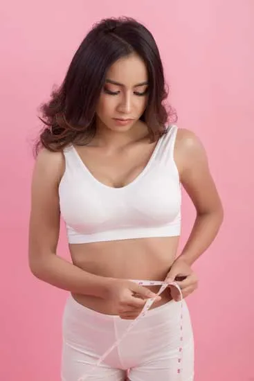Una mujer de pie midiéndose la cintura con un metro, para verificar que no tiene grasa abdominal.