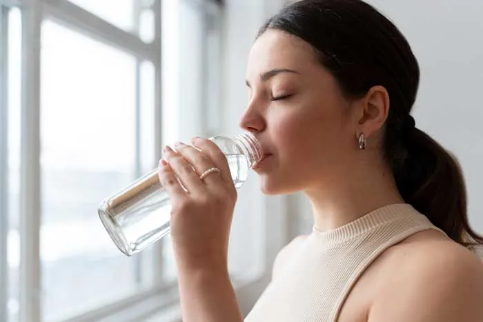 Una mujer bebiendo agua para hidratarse.